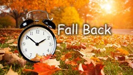 The words Fall Back next to a clock surrounded by fallen leaves.