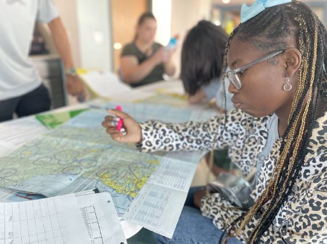 A girl using a pink highlighter to circle different places on a map.