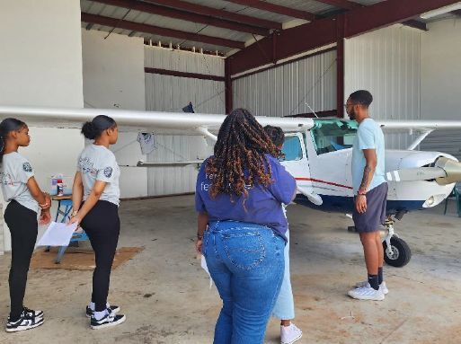 Five individuals standing in an airport hanger looking at an airplane.