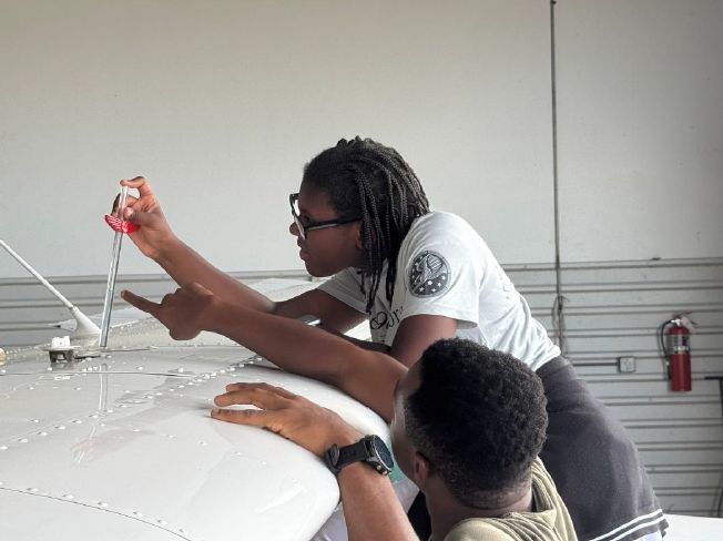 A woman pointing out different spots of an airplane wing to a boy.