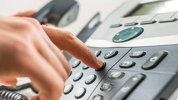 A hand pressing buttons on a corded office phone.