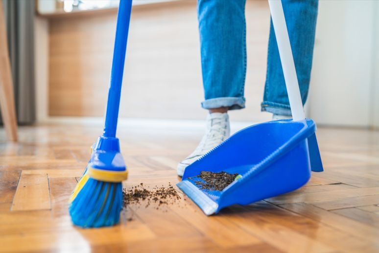 A close-up of a broom pushing dirt into a dustpan.